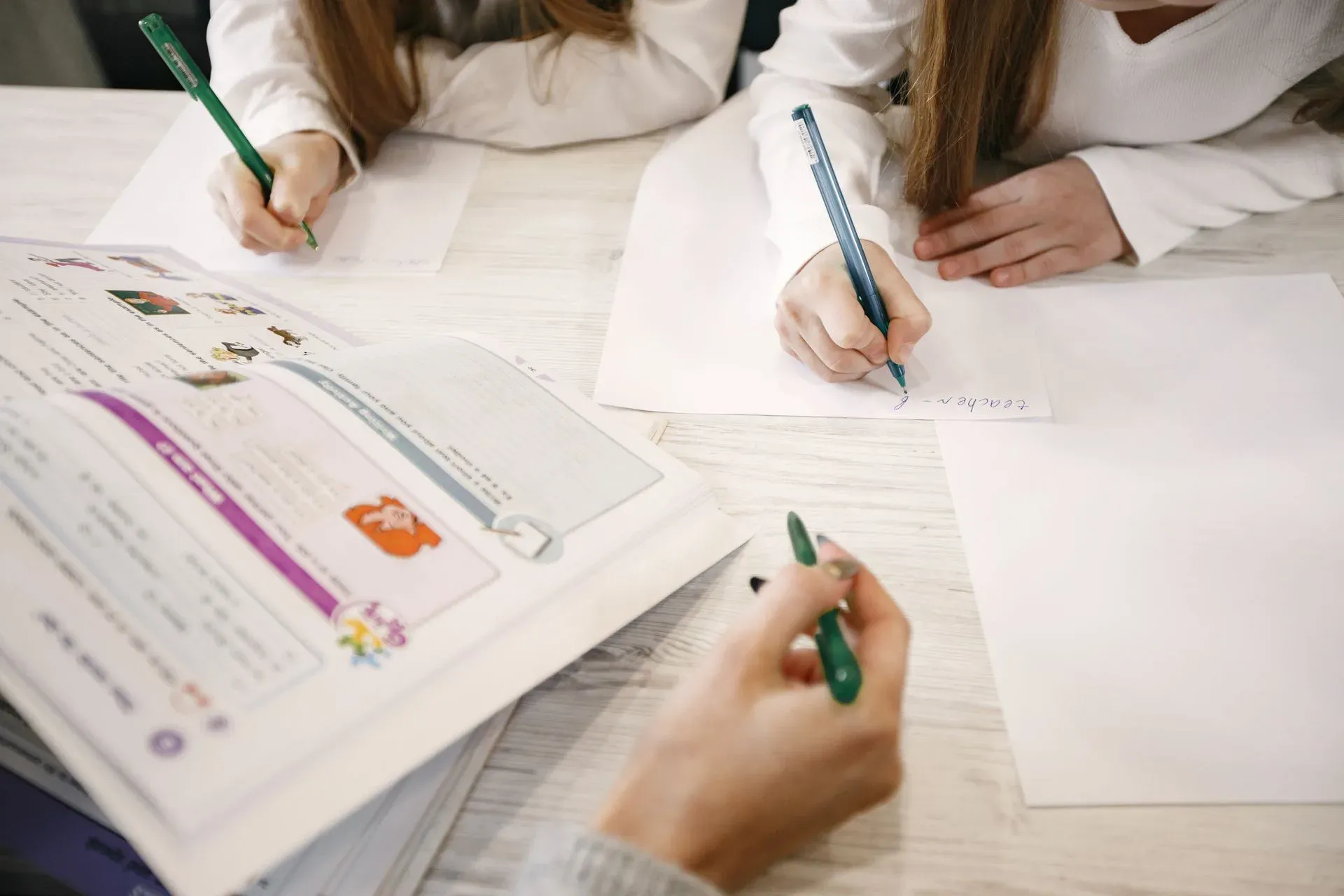 Kinder lernen gemeinsam an einem Tisch, nur Hände die Stifte halten und Bücher sind zu sehen.